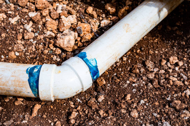 Elbow fitting with blue cement glue join/ bond PVC pipes at bend in dirt trench outdoors for plumbing water drainage installation. Underground irrigation system.