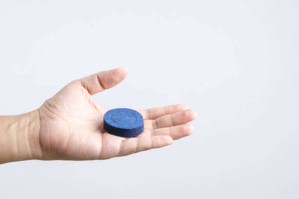Hand holding automatic Bleach toilet bowl cleaner stain remover blue tab or tablet flush tank on white background