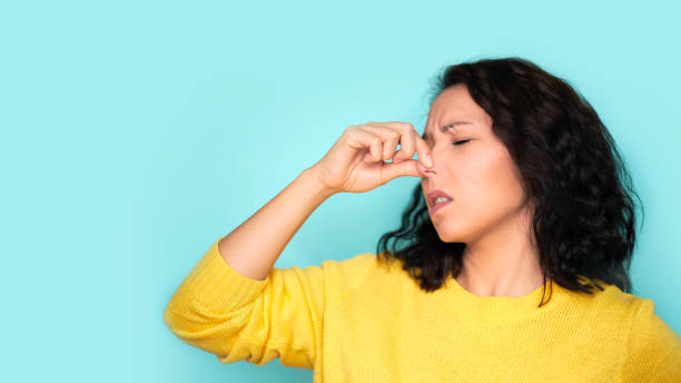 woman smelling something stinky and disgusting, intolerable smell, holding breath with fingers on nose. Bad smells.