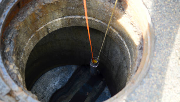 Opening the sewer cover in the middle of the asphalt street. Orange cable on a roll is automatically unrolled in the sewer system for inspection of water congestion